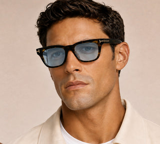 A close-up portrait of a man wearing Tom Ford Havana sunglasses with blue-tinted lenses and gold-tone metal accents on the temples.